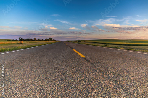 a long remote highway in rural North Dakota with a bright blue sky with clouds in the horizon