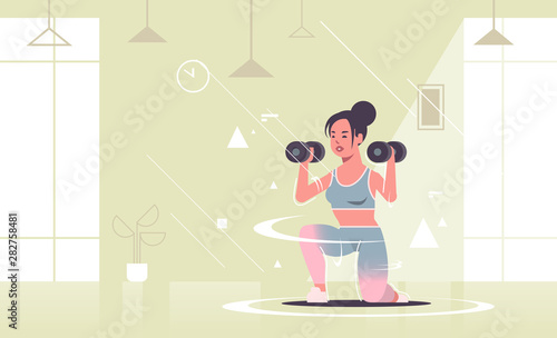 sporty girl doing squats exercises with dumbbells woman training workout healthy lifestyle concept excited sportswoman in sportswear modern gym studio interior flat full length horizontal