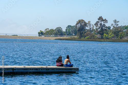 Friends happiness. Yong girls sitting on the wooden pier and having a relax time. Miramare Lake, San Diego, California, USA.