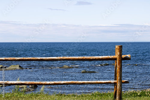 A perch fence in front of the dark blue sea and a light blue sky.