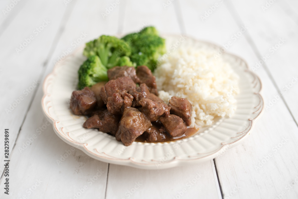 Beef and broccoli Chinese dish over white rice. on a light wood background table Beef and broccoli Chinese dish over white rice. on a light wood background table