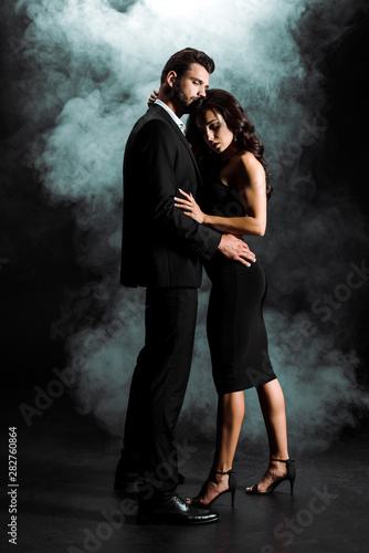 handsome bearded man standing and hugging woman in dress on black with smoke