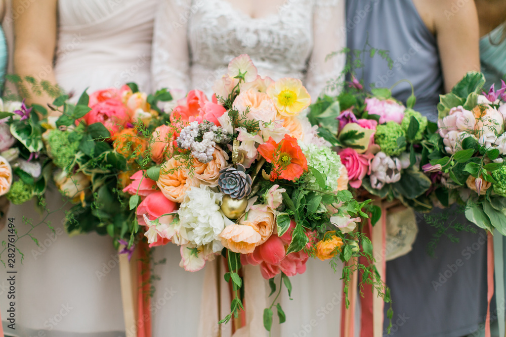 Colorful wedding bouquets, bride and bridesmaids holding wedding flowers, pink and orange ribbons, blue dresses, detail shot Colorful wedding bouquets, bride and bridesmaids holding wedding flowers, pink and orange ribbons, blue dresses, detail shot
