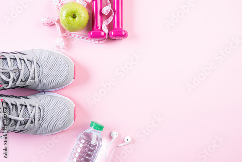 Healthy lifestyle, food and sport concept. Top view of athlete's equipment measuring tape pink dumbbell, sport water bottles, sport shoes and green apple on pink pastel background.