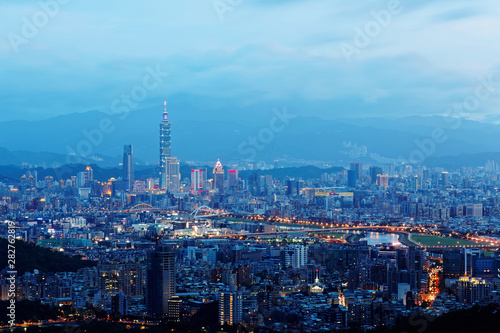 Sunset scenery of Downtown Taipei, vibrant capital city of Taiwan, with landmark tower standing out amid high-rise buildings in Xinyi Financial District & colorful city lights dazzling in twilight