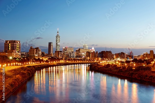 Night view of Taipei City by riverside with skyscrapers and beautiful reflections on smooth water ~ Landmarks of Taipei 101 Tower, Keelung River, Xinyi District and downtown area at dusk