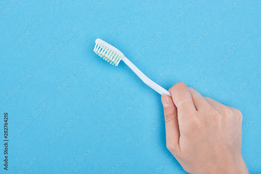 cropped view of woman holding white toothbrush isolated on blue cropped view of woman holding white toothbrush isolated on blue