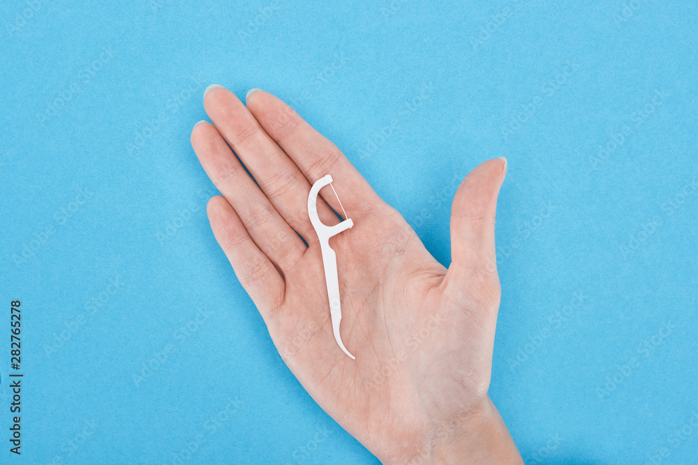 cropped view of woman holding white floss toothpick in hand on blue cropped view of woman holding white floss toothpick in hand on blue