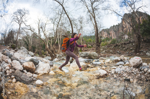 Woman jumps over the mountain river.