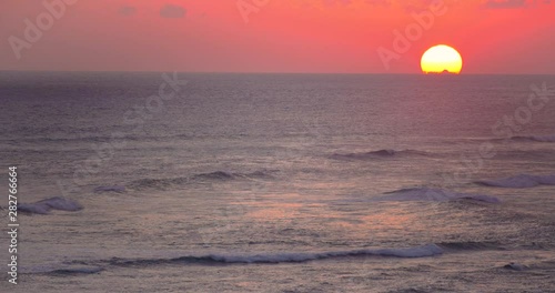 Calm and relaxing view of golden sun setting below horizon and slow moving waves, Indonesia