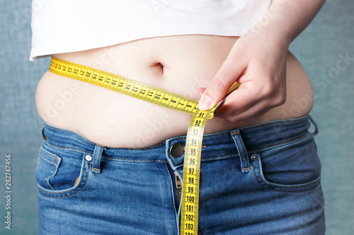 Woman's hand measure her stomach with a tape measures, overweight concept photo