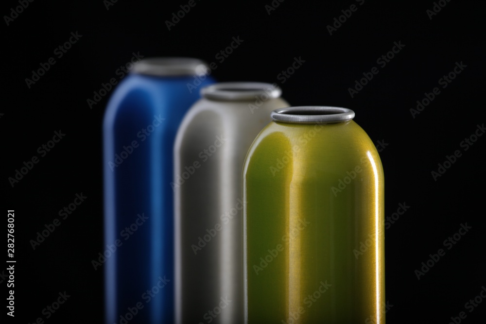 3 aluminum aerosol cans in blue, gray, and yellow, located in front of a black background. the boxes are in the raw form and in a row in a row.
