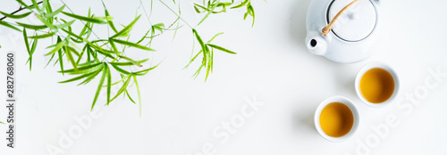 Asian tea concept, two white cups of tea and teapot surrounded with green tea...