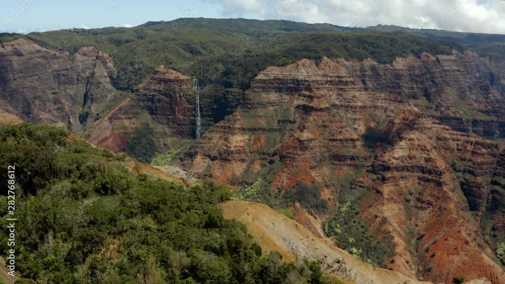 Massive canyon with rugged cliffs and luscious green trees. A waterfall is present in the distance. Aerial 4K drone shot flying towards the canyon. Massive canyon with rugged cliffs and luscious green trees. A waterfall is present in the distance. Aerial 4K drone shot flying towards the canyon.