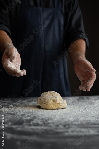 Fototapeta Naklejka Na Ścianę i Meble -  kitchen table, a piece of fresh raw dough, flour sprinkled, chef's male hands