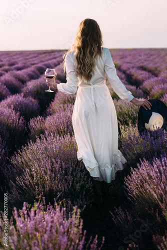 Picnic in nature, a young beautiful girl stands on a lavender field, a glass of wine, female hands