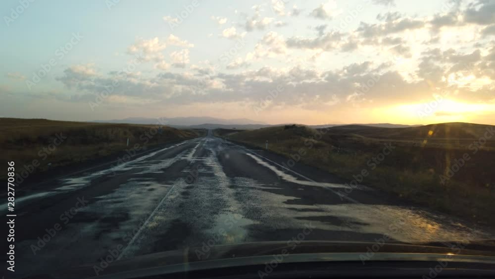Slow Motion:View from inside car on empty hilly road leading to horizon line at sunset or sunrise Slow Motion:View from inside car on empty hilly road leading to horizon line at sunset or sunrise