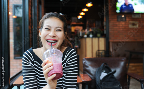 Asian women enjoy drinking smoothie frappe in cafe,Asian girl Smile while wearing braces,selective focus