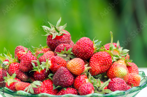 Freshly Harvested Red Strawberries In A Glass Bowl on Blurred Green Background. Organic Farming  Healthy Food Concept.