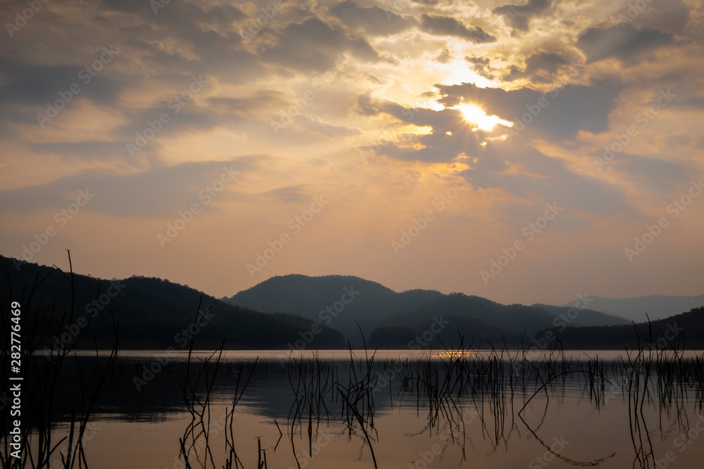 Landscape of the sun shining through cloudy sky over the lake with crystal clear water and mountains at a national park during sunrise. 