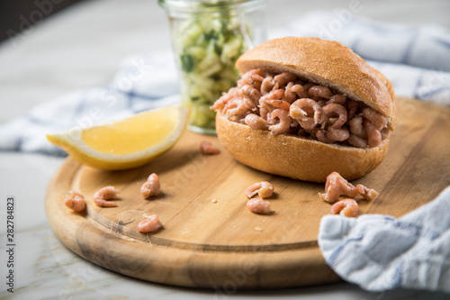 Nordseekrabben Brötchen als Fischbrötchen mit Gurkensalat und Zitrone auf Holz Brett und Marmor Tisch