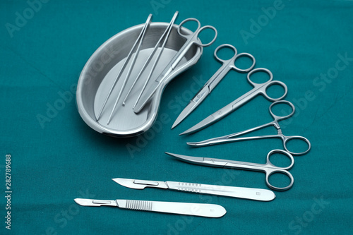 Basic surgical instrument forceps tweezers scissors in emesis or plus basin and scalpel on surgical green drape fabric