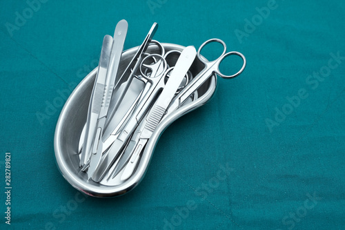 Basic surgical instrument scalpel forceps tweezers scissors in emesis or plus basin  on surgical green drape fabric photo