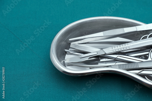 Basic surgical instrument scalpel forceps tweezers scissors in emesis or plus basin  on surgical green drape fabric