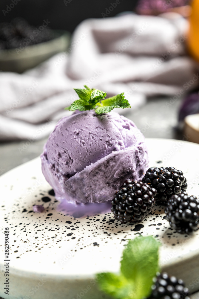 Berry ice cream. Decorated with blackberries and mint leaves. Ceramic plate. Gray concrete background.