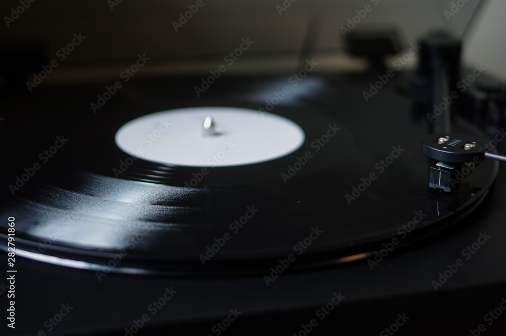 Modern round headshell with cartridge on straight tonearm and vinyl record disc with white label spinning on belt drive turntable Modern round headshell with cartridge on straight tonearm and vinyl record disc with white label spinning on belt drive turntable