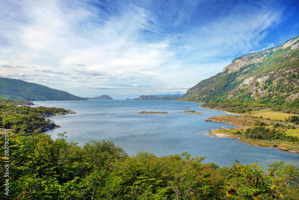 Panoramic view of Tierra del Fuego National Park, showing small islands surrounded by green vegetation and water, against a blue sky.