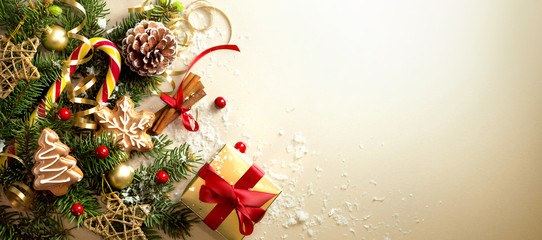 Christmas decoration composition on light gold background with beautiful Golden gift box with red ribbon, fir branches, cones, stars, Christmas cookies,cinnamon, top view, copy space, banner format.