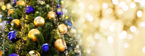 Christmas tree decorated with Golden and blue balls toys on a blurred, sparkling and fabulous fairy background with beautiful bokeh, copy space, banner format. © Laura Pashkevich