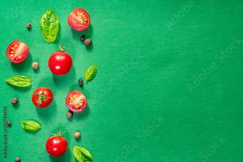 Halved Juicy Cherry Tomatoes and Basil Leaves on a green background. Concept for healthy nutrition. Top view. Copy space.