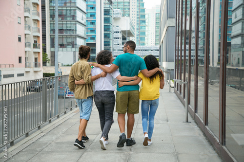 Group of close friends spending leisure time together. Rear view of mix raced people walking down urban street, embracing each other and talking. Friendship concept