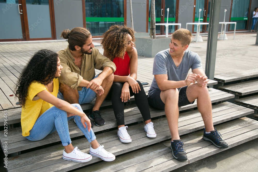 Group of friends sitting on staircase together and chatting. Mix raced team of young people sitting outside and talking to each other. Meeting outdoors concept Group of friends sitting on staircase together and chatting. Mix raced team of young people sitting outside and talking to each other. Meeting outdoors concept