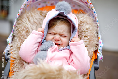 Картината върху платно Sad crying little beautiful baby girl sitting in the pram or stroller on autumn day