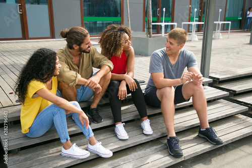Fototapeta Naklejka Na Ścianę i Meble -  Group of friends sitting on staircase together and chatting. Mix raced team of young people sitting outside and talking to each other. Meeting outdoors concept