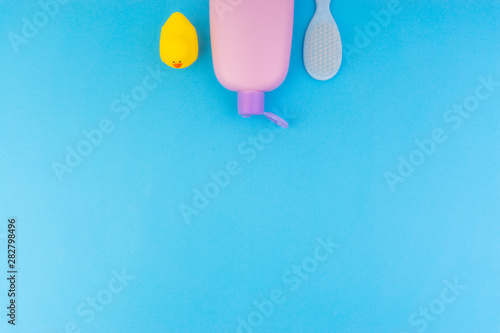 Flat lay composition of baby care products on a blue background. View from above shampoo or shower bottle gel, cleaning brush and yellow rubber toy duck