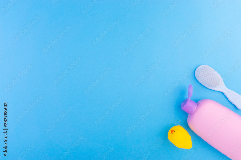 Flat lay composition of baby care products on a blue background. View from above shampoo or shower bottle gel, cleaning brush and yellow rubber toy duck Flat lay composition of baby care products on a blue background. View from above shampoo or shower bottle gel, cleaning brush and yellow rubber toy duck