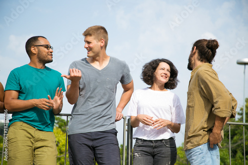 Happy people chatting on bridge. Interracial group of people standing outdoors, leaning on railing, talking, arguing, laughing. Tourists outdoors concept