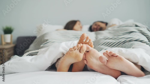 Man and woman couple are lying in bed touching feet talking enjoying bedtime together in cosy bedroom. Relationship, relaxation and apartment concept. photo