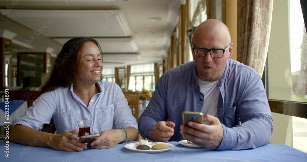 Internet addicted cheerful married couple sitting in a restaurant drinking tea from Oriental glasses and eating desserts sweets. Discuss online news Internet addicted cheerful married couple sitting in a restaurant drinking tea from Oriental glasses and eating desserts sweets. Discuss online news