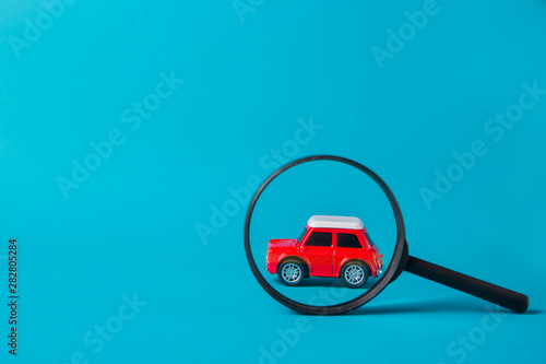 Red car peeked out with a magnifying glass on blue background. Technical inspection and machine search concept photo