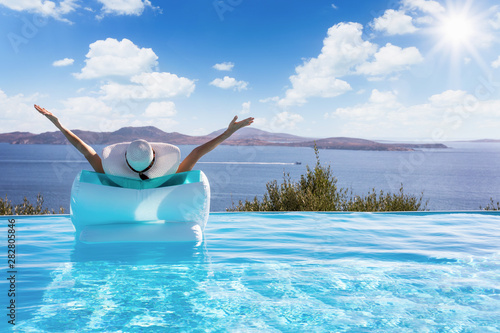 Sommerurlaub Konzeot: Frau auf einer Luftmatratze im Infinity Pool streckt vor Freude die Arme in die Luft und genießt die Aussicht auf das Meer photo