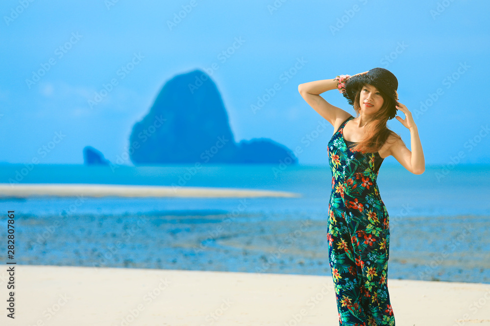 Young woman in summer dress standing on sand and holding straw hat looking to a sky Young woman in summer dress standing on sand and holding straw hat looking to a sky