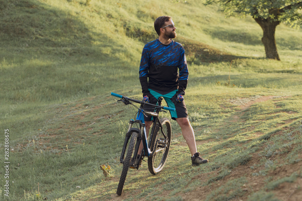 Fototapeta premium Cyclist in shorts and jersey on a modern carbon hardtail bike with an air suspension fork rides off-road on the orange-red hills at sunset evening in summer 