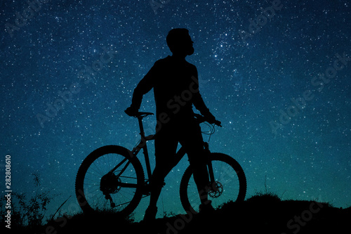 Cyclist in shorts and jersey on a modern carbon hardtail bike with an air suspension fork rides off-road on the orange-red hills at sunset evening in summer 