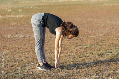 Slim sports girl performs leg stretching exercises on the nature.