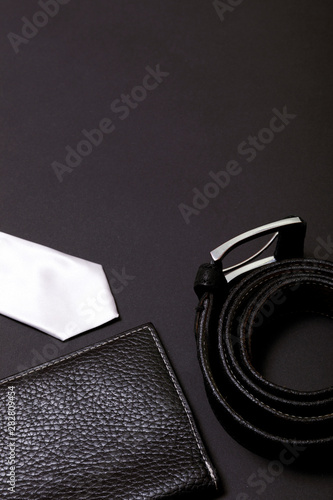 White men's tie and a leather belt with a couple on black background, top view. 
